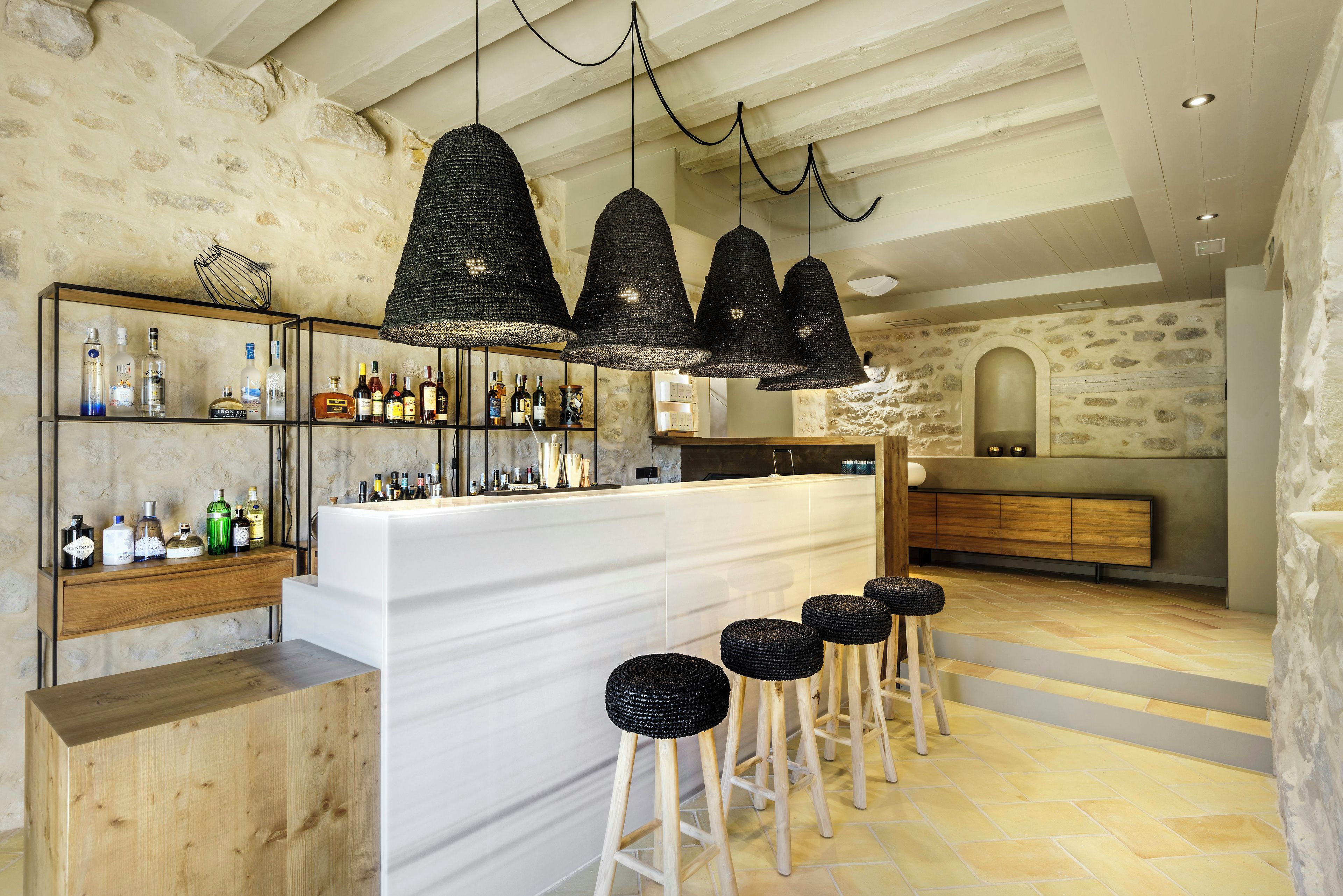 A bar area with a white counter, black woven pendant lights, and stools.