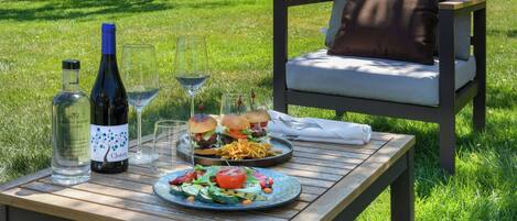 A picnic setup with a bottle of wine, glasses, a plate of food, and a chair.