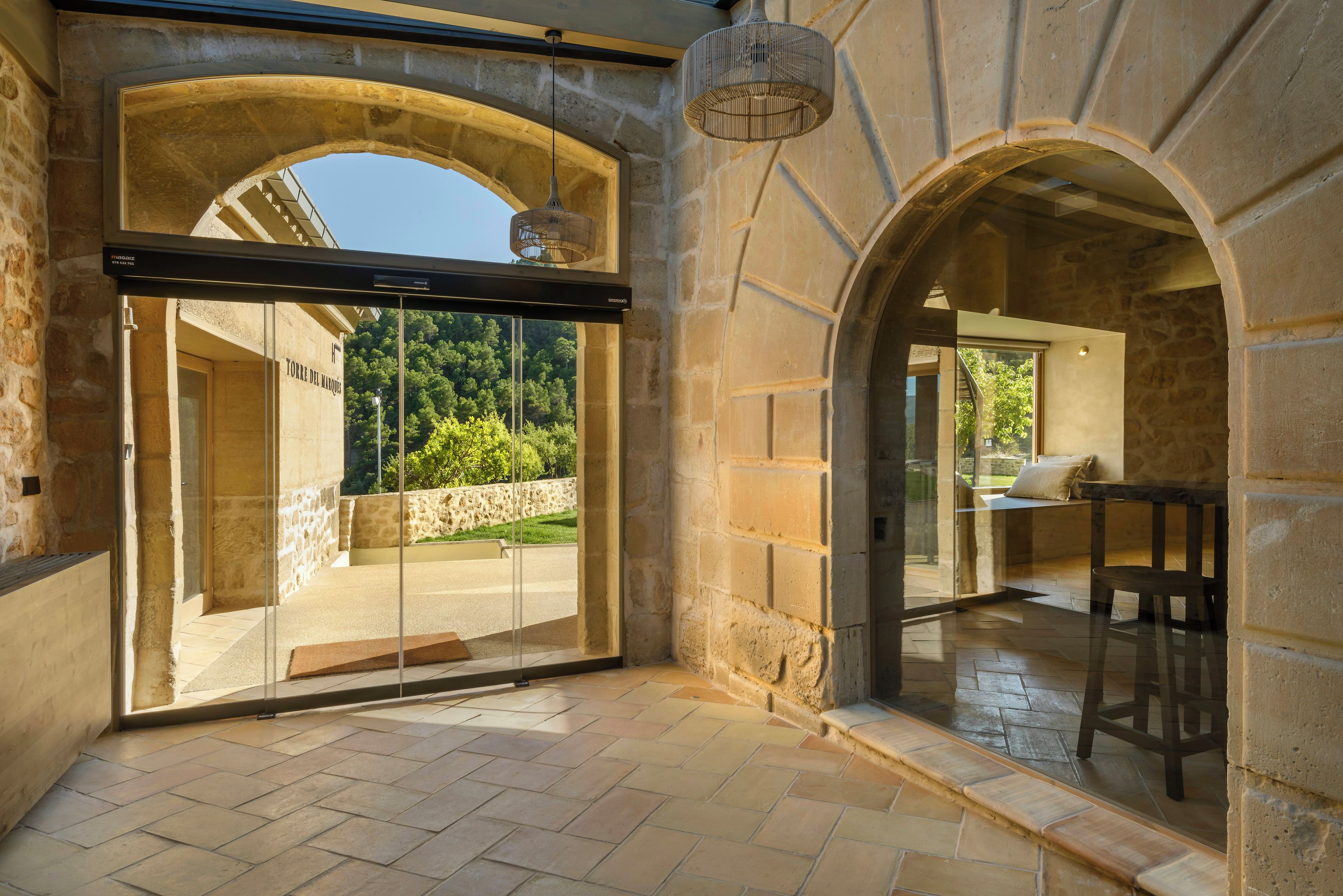 A stone-walled room with a glass door leading to an outdoor area, a hanging light fixture, and a stone bench.