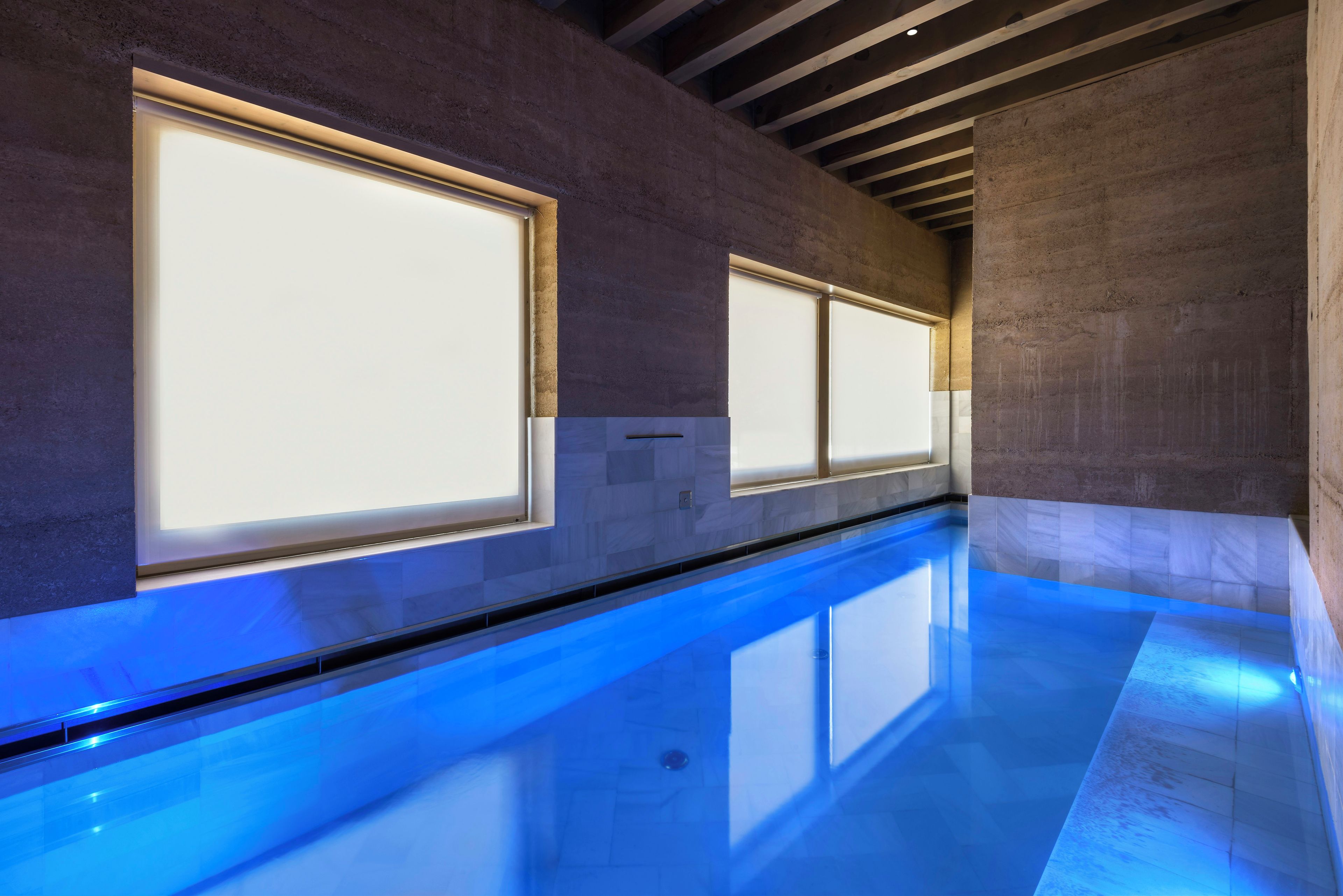 Una piscina interior moderna con paredes de vidrio transparente y suelo iluminado en azul.