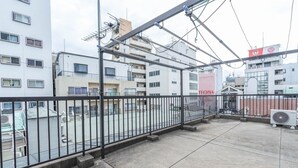 A rooftop terrace with a metal railing, air conditioning units, and a view of surrounding buildings. - Apartment Y Kawara Heights Namba (Osaka)