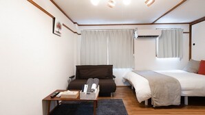 A compact hotel room with a bed, a sofa, a small table, and a window with curtains. - Apartment Y Kawara Heights Namba (Osaka)