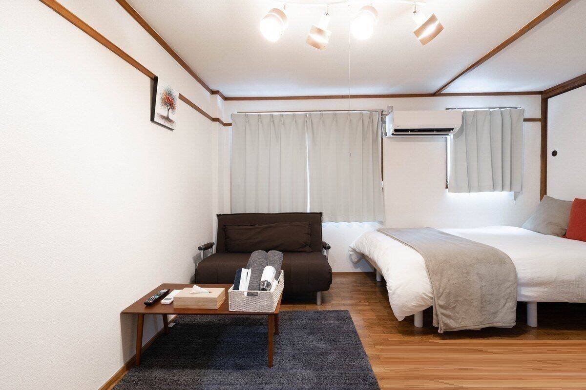 A compact hotel room with a bed, a sofa, a small table, and a window with curtains.