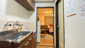 A compact kitchen with a sink, cabinets, and a refrigerator. A hallway leads to a bedroom with a bed and a window. - Apartment Y Kawara Heights Namba (Osaka)