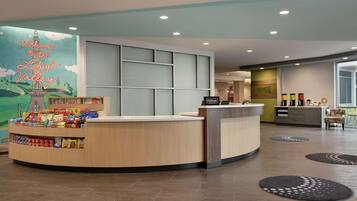 A hotel reception area with a counter displaying snacks and a neon sign welcoming guests to the hotel.