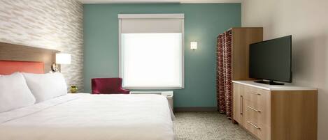 Una habitación de hotel con una cama, un televisor sobre un mueble de madera, una ventana con cortinas y una silla roja.