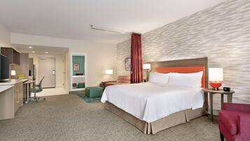 A hotel room with a bed, desk, chair, and a small table with a lamp.