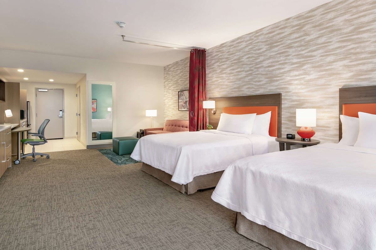 Ein Hotelzimmer mit zwei Betten, einem Schreibtisch, einem Stuhl und einer kleinen Sitzecke.