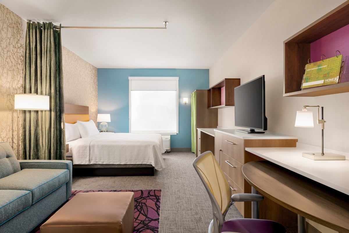 Ein Hotelzimmer mit einem Bett, einem Schreibtisch, einem Sessel, einem Fernseher und einem Fenster.