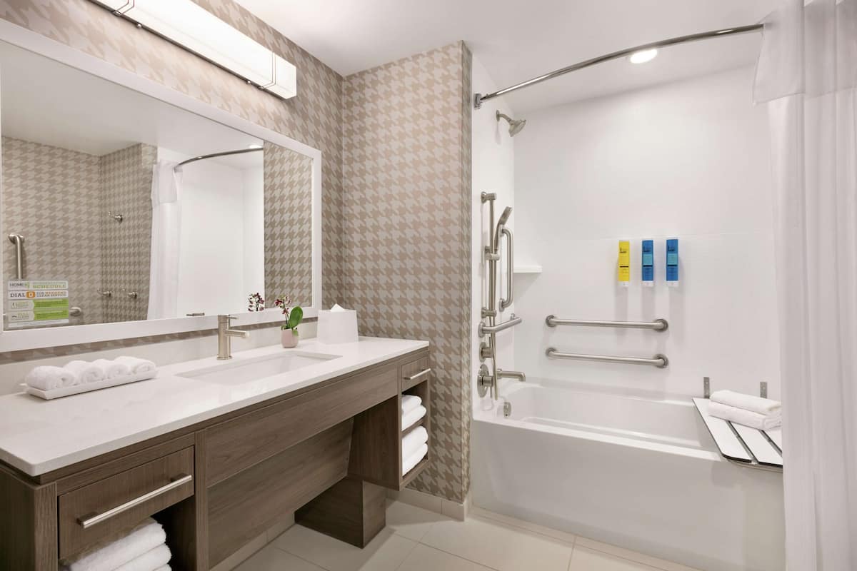 Ein modernes Badezimmer mit einem Doppelwaschtisch, einem großen Spiegel, einer Dusche mit Glastür und Pflegeprodukten an der Wand.
