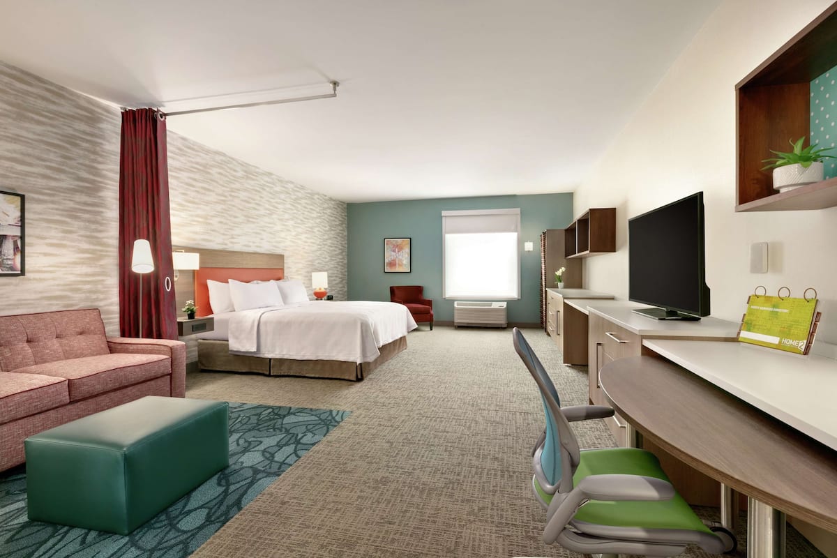 Ein Hotelzimmer mit Bett, Schreibtisch, Fernseher und einer Couch.