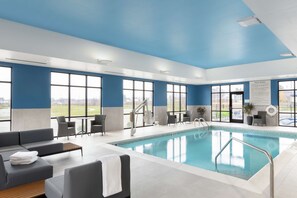 A modern indoor pool area with a blue ceiling, large windows, and a pool with a metal ladder.