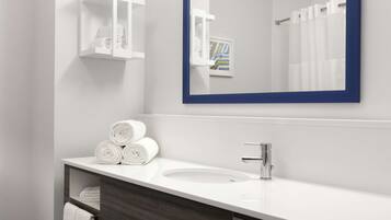 A modern bathroom with a white sink, dark wooden vanity, a mirror with a blue frame, and a towel rack with rolled towels.