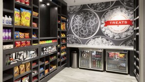 Un rayon dédié aux collations et aux gourmandises, avec des étagères remplies de divers produits, une pancarte indiquant « Bienvenue dans notre magasin » et une autre pancarte indiquant « Gourmandises ».