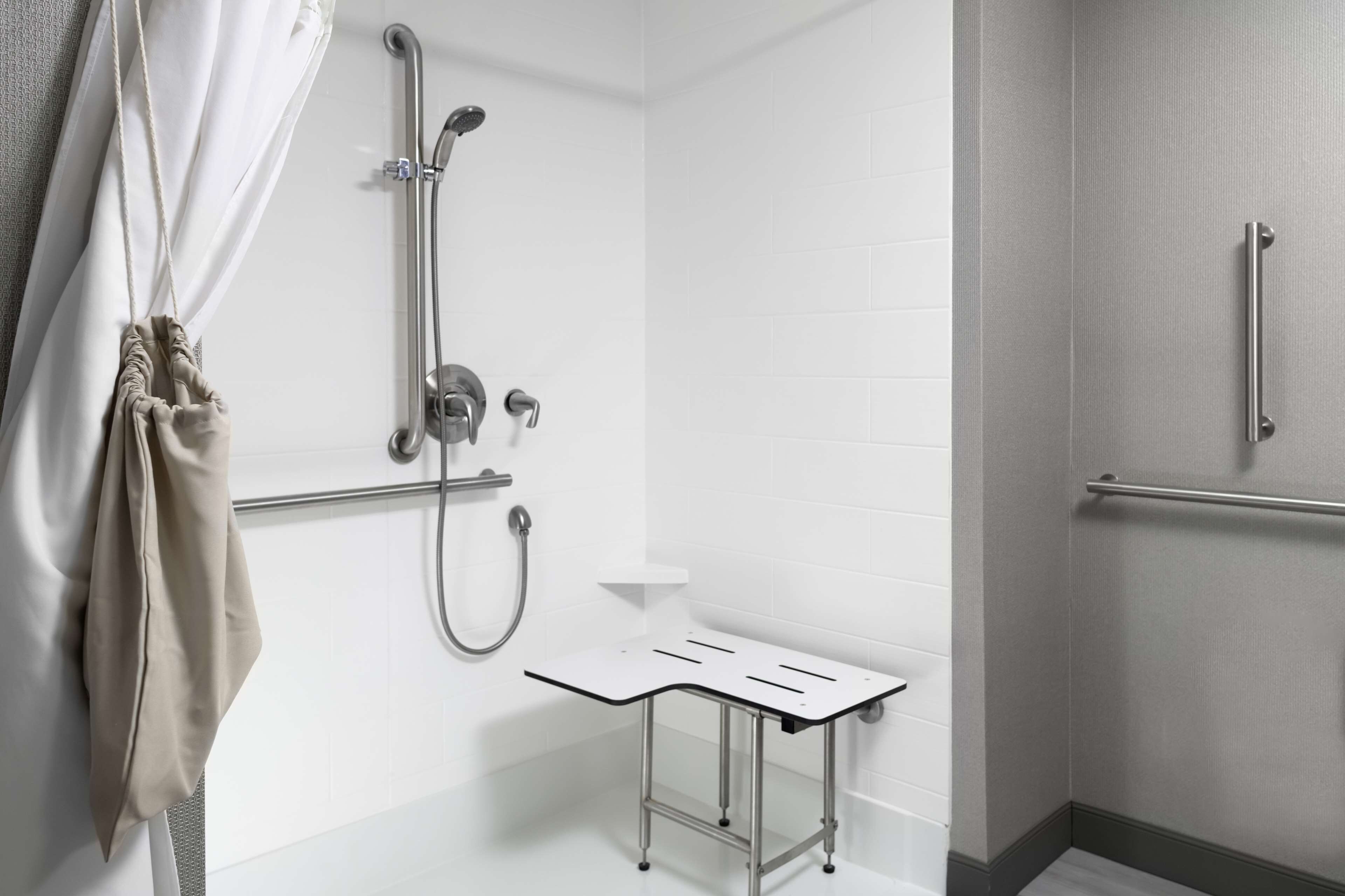 A modern bathroom with a shower, grab bars, and a small table.