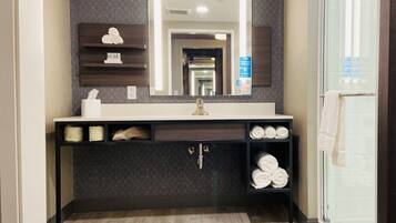 Une salle de bain moderne avec un grand miroir, des carreaux à motifs foncés, un lavabo blanc et une douche en verre.