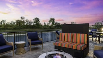 Een terras met rieten meubels, een ronde tafel en een vuurkorf.