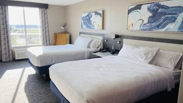 A hotel room with two beds, a large window with curtains, and abstract art on the walls.