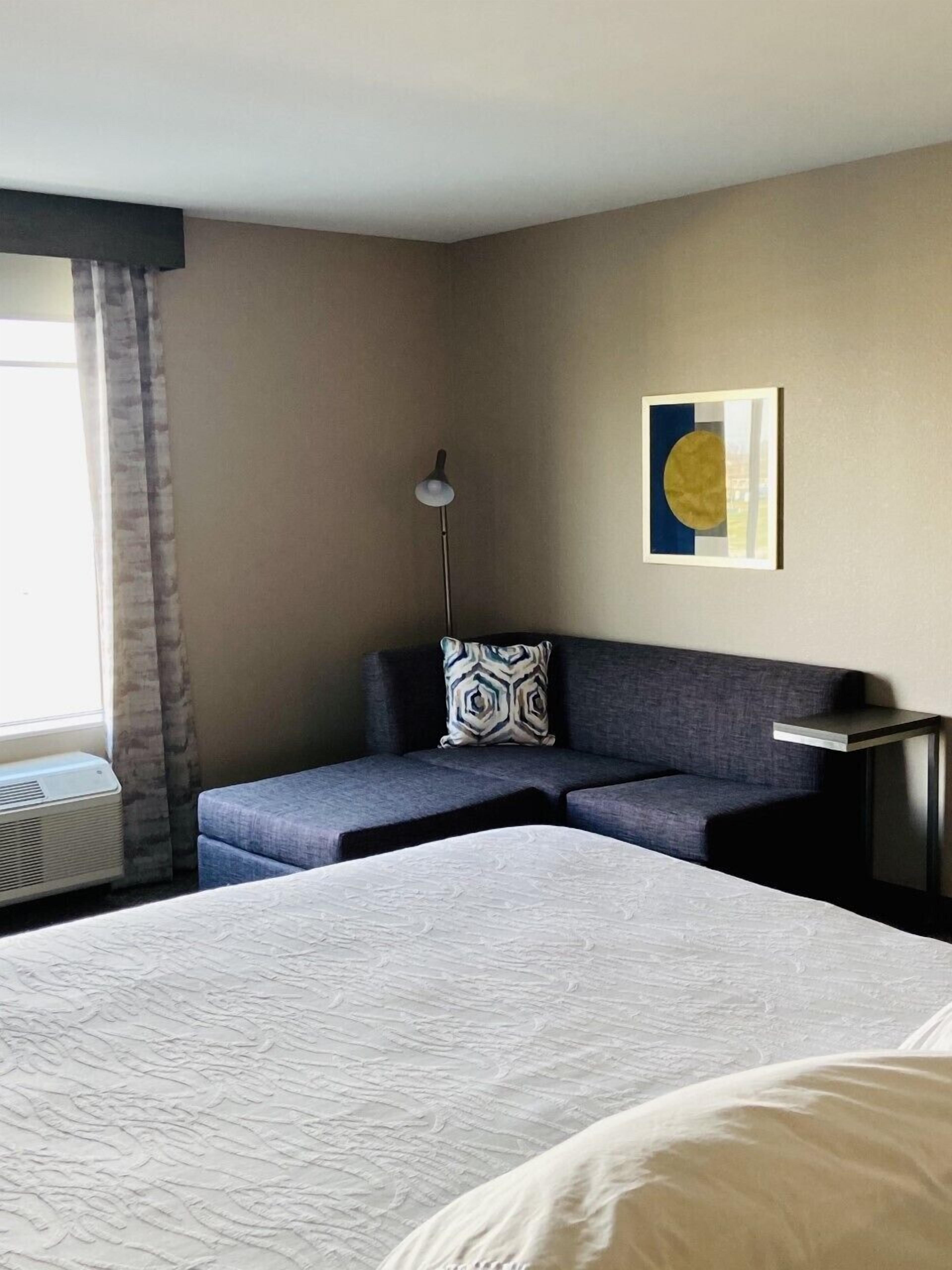 Habitación de hotel con una cama grande, un sofá, una lámpara de pie y un cuadro en la pared.