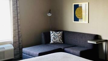 Habitación de hotel con una cama grande, un sofá, una lámpara de pie y un cuadro en la pared.
