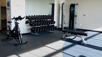 A gym with exercise equipment, including a stationary bike, dumbbells, a bench, and a squat rack.