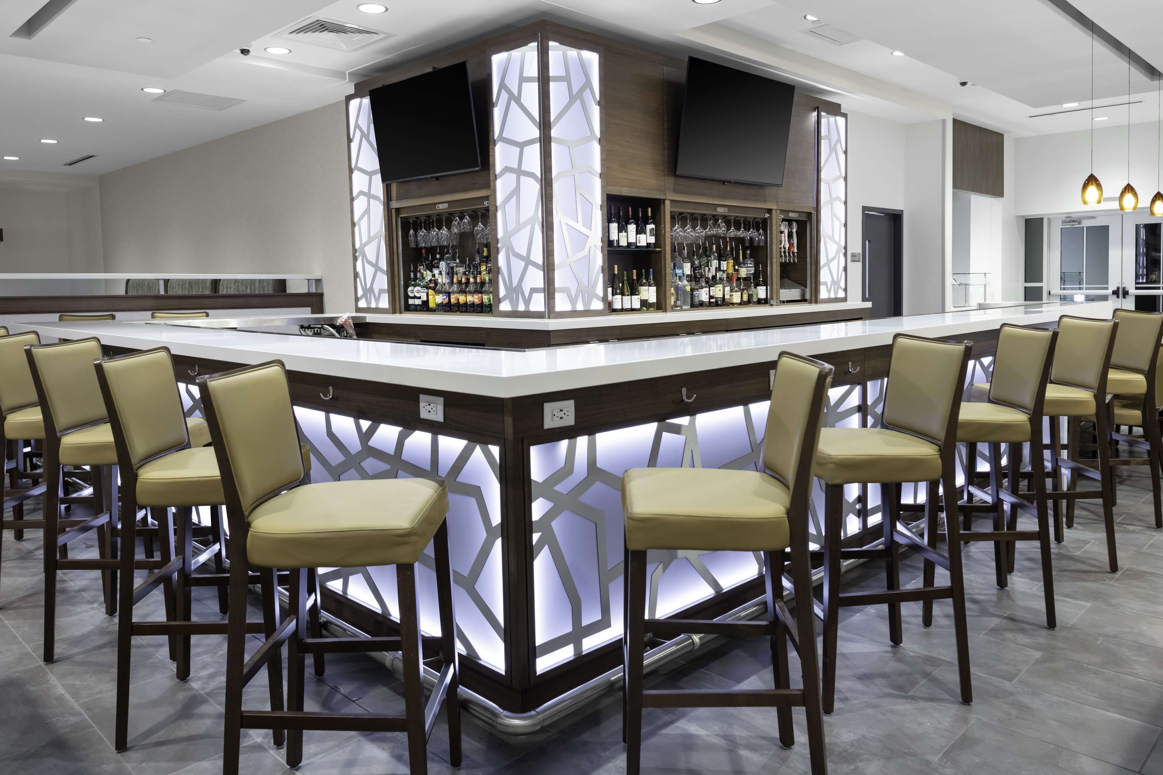 A modern bar area with a central island, bar stools, and a well-stocked liquor shelf.