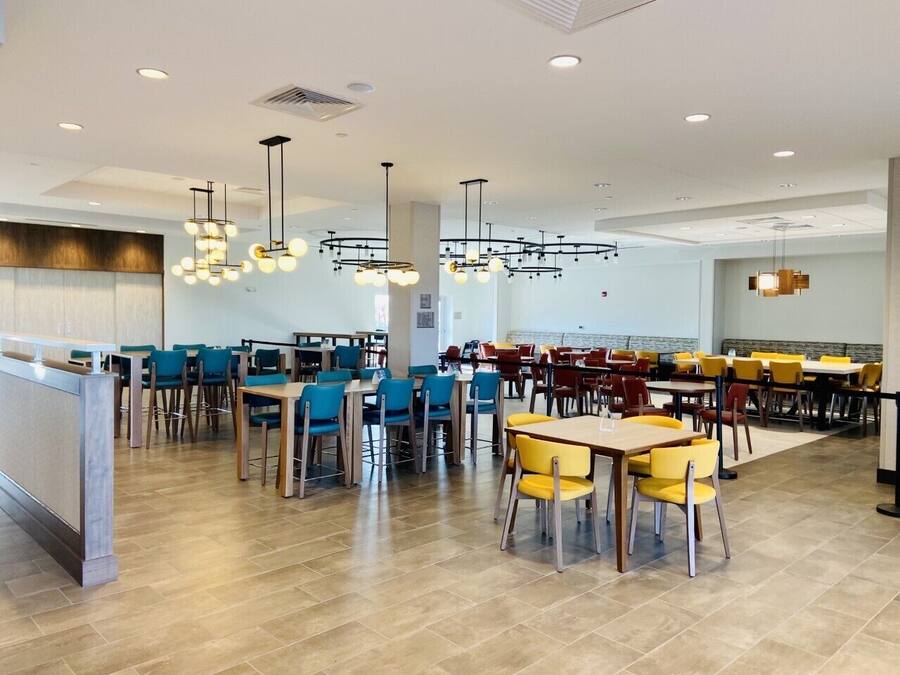 A spacious cafeteria with multiple dining tables and chairs, featuring a modern design with pendant lighting.