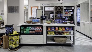 A modern retail area with a coffee station, snack shelves, and refrigerated sections labeled 'CHILLED' and 'FROZEN'. - Home2 Suites by Hilton Fort Wayne North (Fort Wayne)
