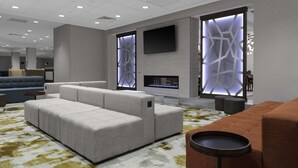 A modern living room with a sectional sofa, a fireplace, and a flat-screen TV mounted on the wall. - Home2 Suites by Hilton Fort Wayne North (Fort Wayne)