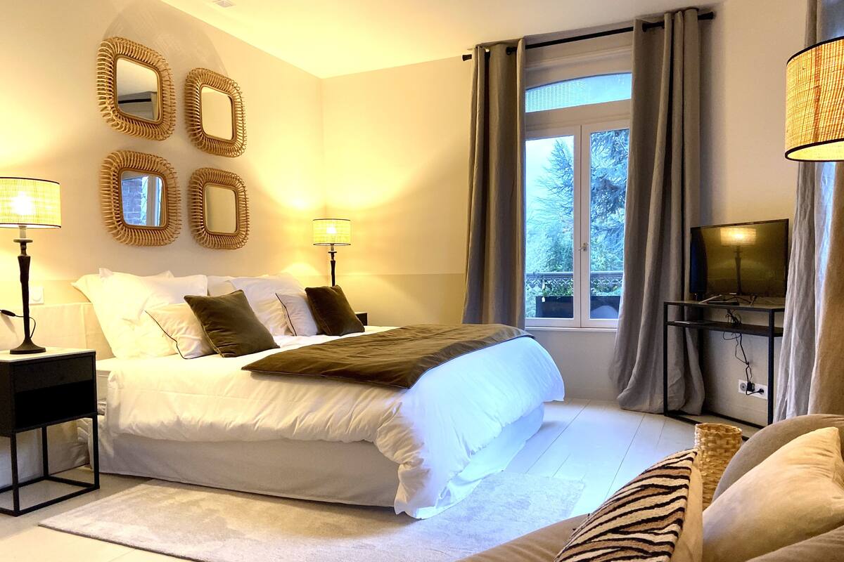 Quarto com cama, mesas de cabeceira, luminárias, televisão e janela com cortinas.