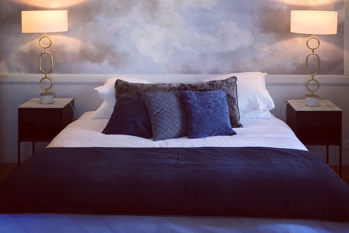 Quarto com cama, duas mesas de cabeceira e um grande mural temático de nuvens.