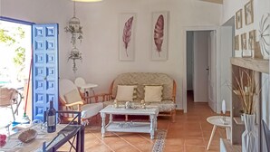 Een gezellige woonkamer met een bank, salontafel en stoelen. Er zijn decoratieve veren aan de muur en een hangende vogelkooi met planten.