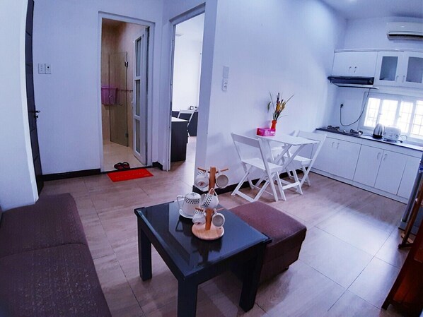 Un salon moderne avec une table basse noire, des chaises blanches et un coin cuisine doté de meubles blancs et d’une cuisinière.