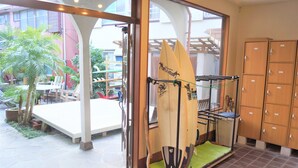 A room with a surfboard rack, a small seating area with a table and chairs, and a view of the outside. - Resort Pension Turtle House (Shimoda)