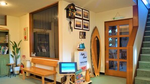 A room with a wooden bench, a small table with a computer, a wall clock, framed pictures, and a sign that reads "Coffee, Snack, Turtle House, Beach, Surf, Sand Bar." - Resort Pension Turtle House (Shimoda)