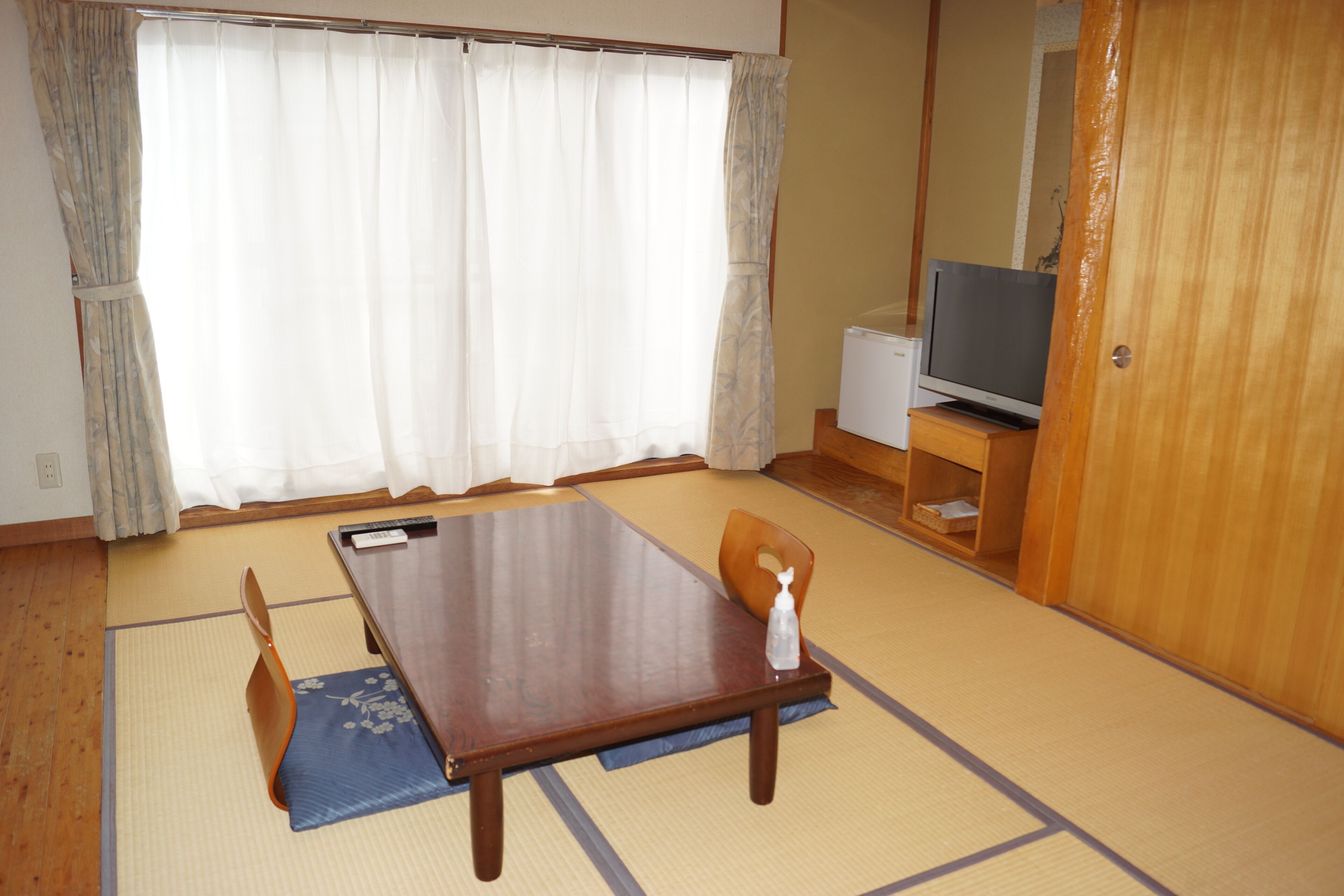 A traditional Japanese room with tatami flooring, a low wooden table, a television, and a sliding door.