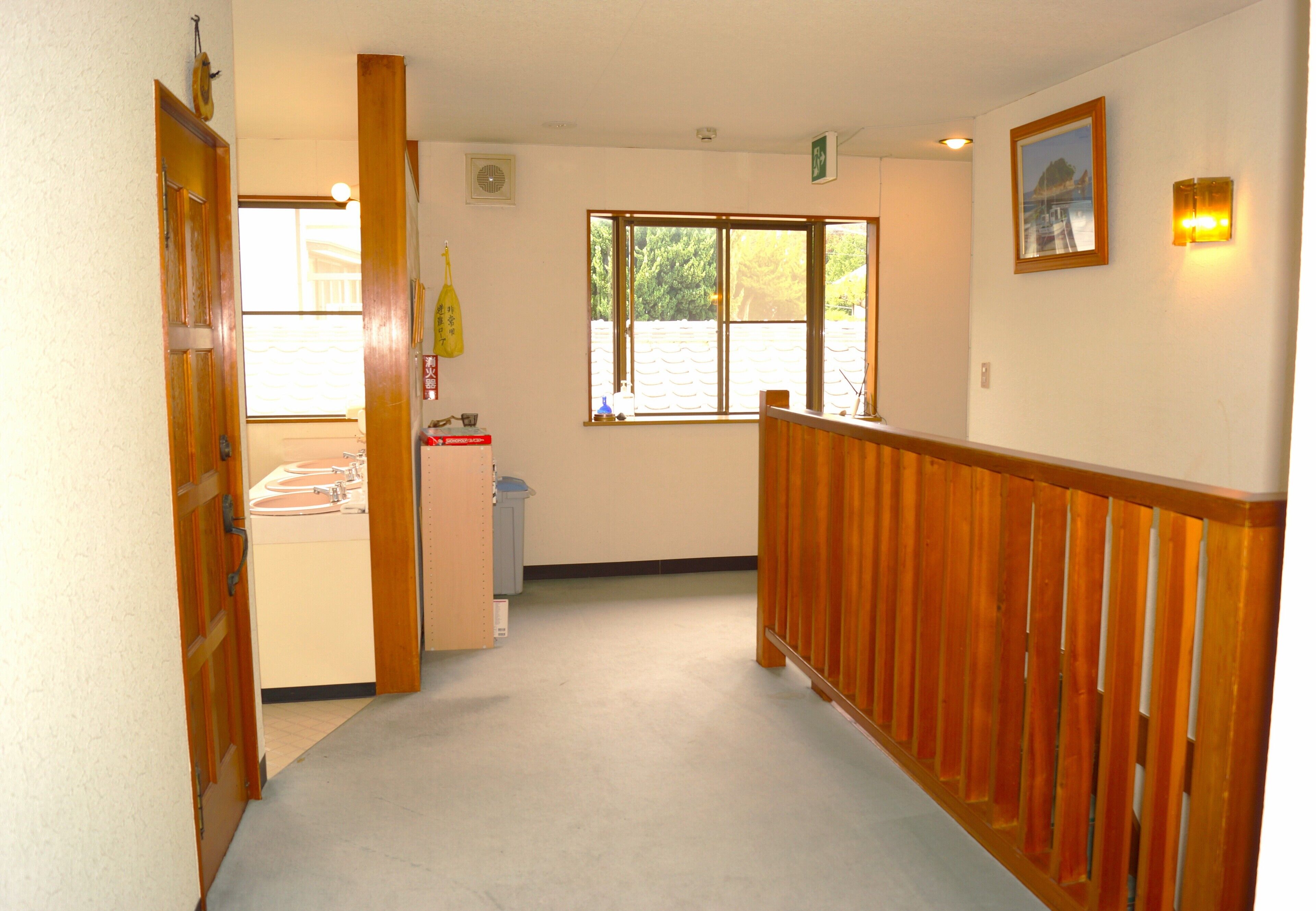A hallway with a wooden railing, a window with a view of greenery, and a door leading to a bathroom.