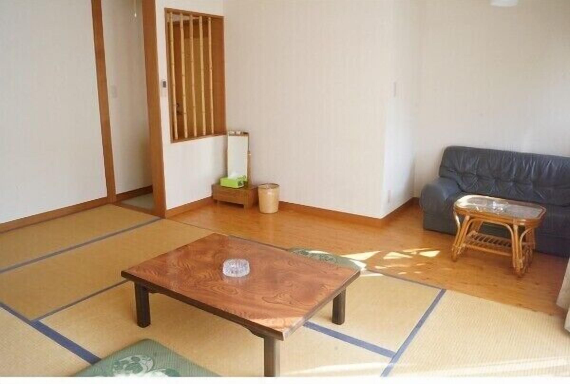 A room with tatami flooring, a wooden table, a grey sofa, and a small stool.