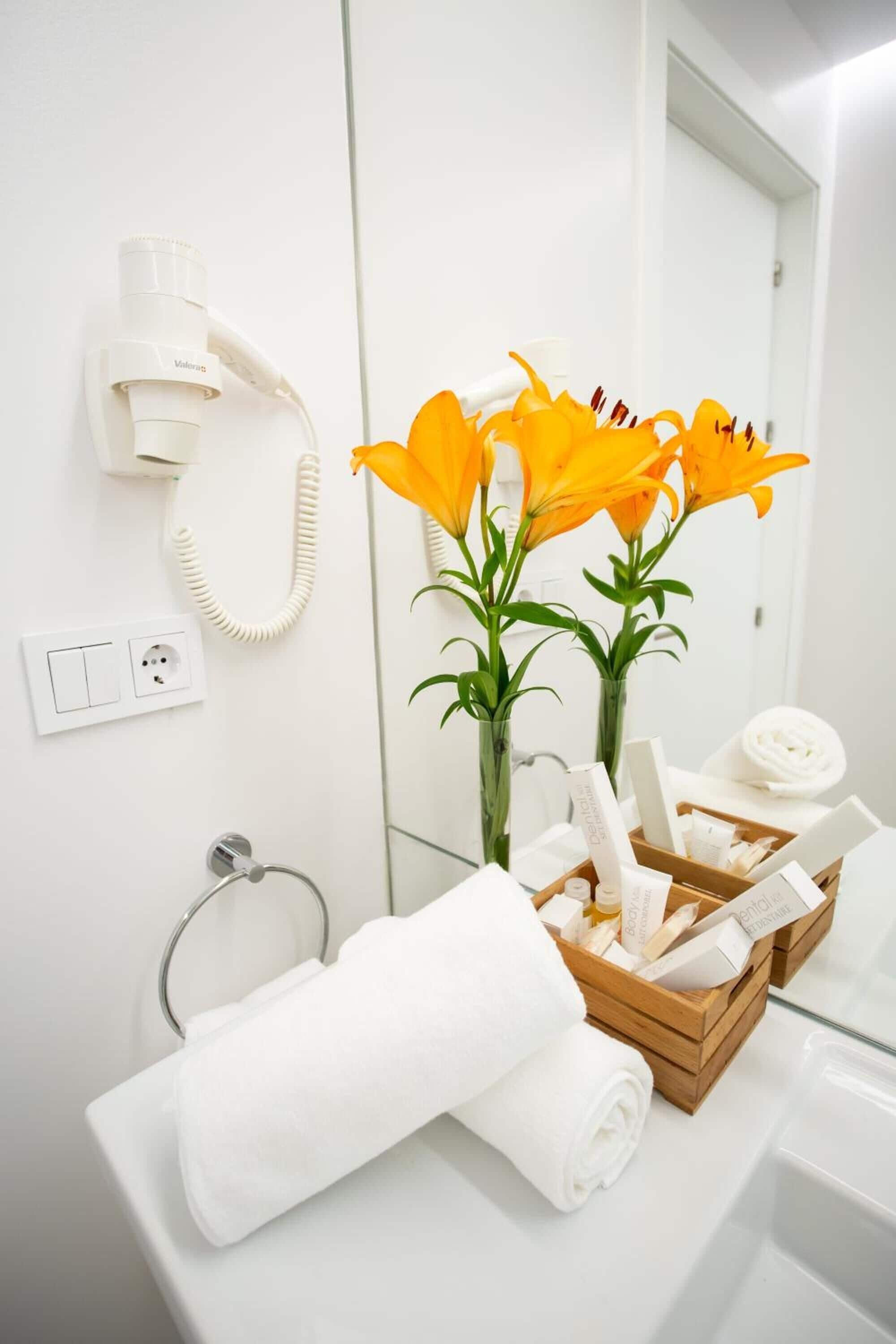 A bathroom with a white sink, a mirror, a telephone, and a wooden tray with toiletries.