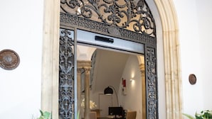 An ornate entrance with a decorative metal gate, a dining area with a table and chairs, and potted plants. - Plazuela del Carbón Suites (Cádiz)