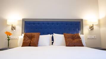 Una habitación de hotel con una cama grande, dos mesitas de noche y una mesita auxiliar con una lámpara.