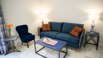 A living room with a blue sofa, two side tables with lamps, a blue chair, and a coffee table with a book and glasses.