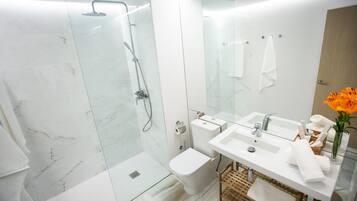 A modern bathroom with a glass-enclosed shower, a toilet, a bidet, a sink with a mirror, and a small wicker basket.