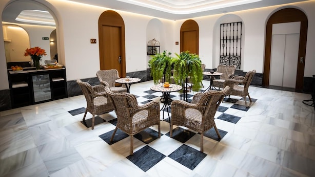 A lobby with a checkered floor, wicker furniture, and potted plants. - Plazuela del Carbón Suites (Cádiz)