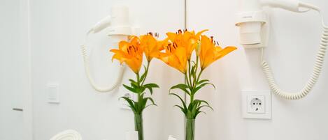 A bathroom with a white sink, a mirror, a hairdryer, a towel, and a vase with flowers.