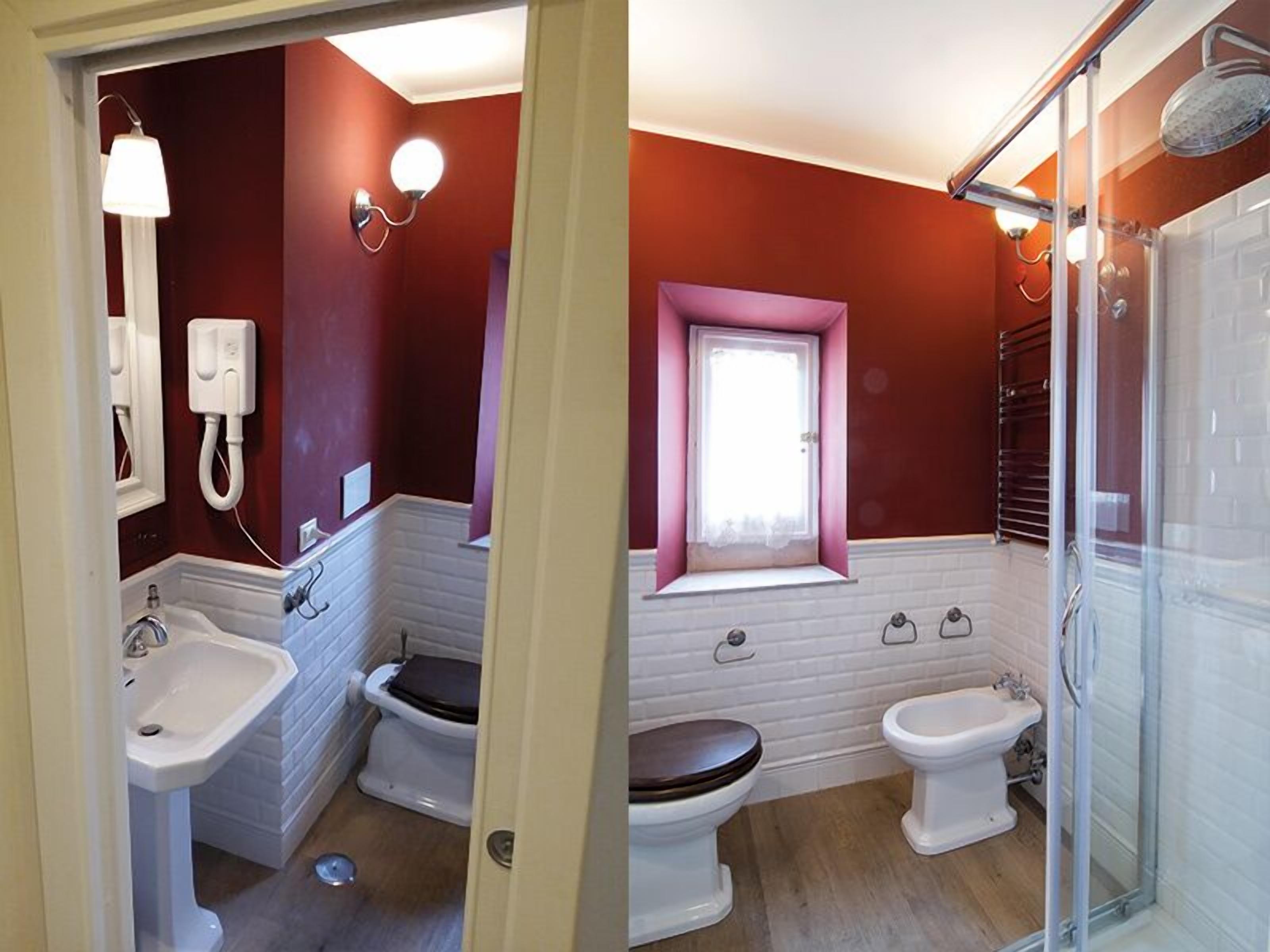 Une salle de bain avec un lavabo blanc, deux toilettes, une douche et une fenêtre à cadre blanc.