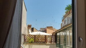 Blick aus einem Fenster eines Wohnhauses mit Balkon, Klimaanlagen und einer Tür.