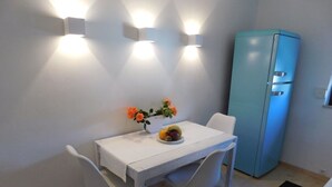 A small dining area with a white table, two white chairs, a blue refrigerator, and wall-mounted lights. - Private apartment Angelika NEW (Lorch)