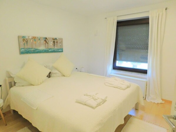 A bedroom with a bed, pillows, a painting, a window with curtains, and a towel on the bed. - Private apartment Angelika NEW (Lorch)