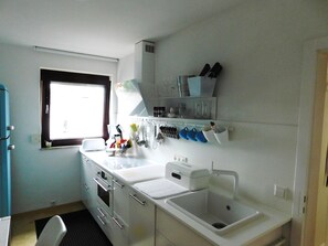 Una piccola cucina con una finestra, mobili bianchi, un lavello e diversi utensili ed elettrodomestici.